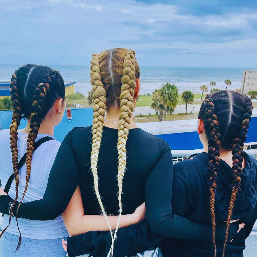 three individuals with long feed in dutch braid hairstyles standing on a balcony overlooking the ocean and beach in Daytona Beach