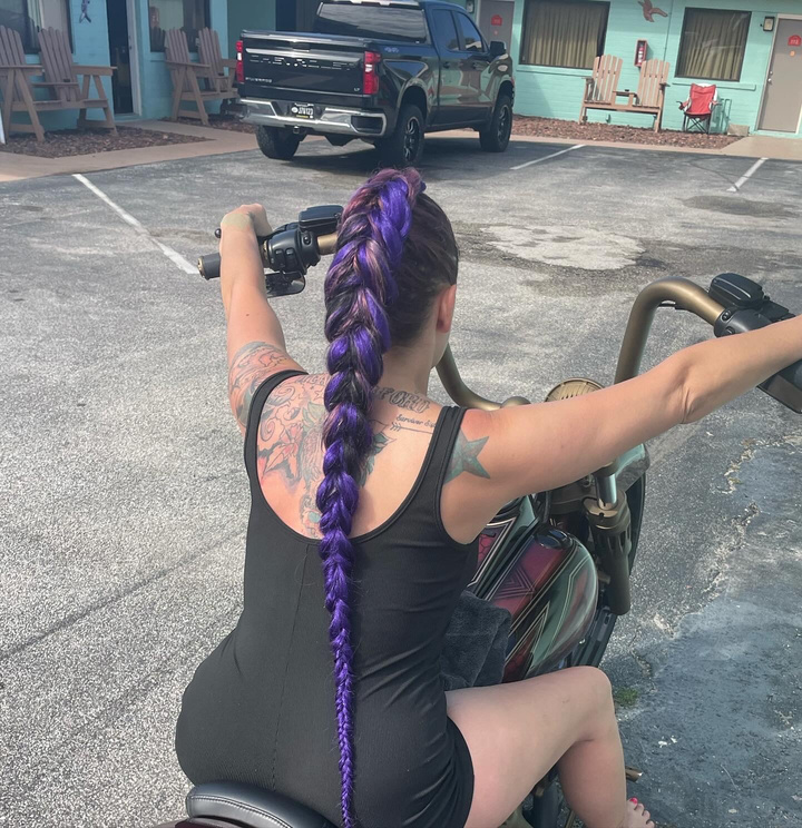 A person with purple hair braided sitting on a motorcycle in daytona beach